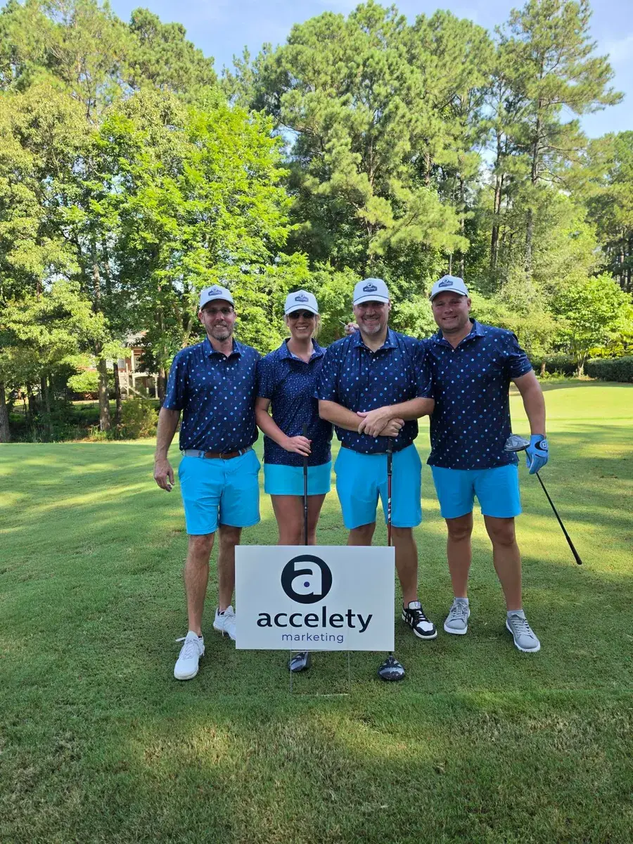 Team on a golf course beside an Accelety sign